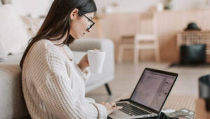 Foto de uma mulher usando um laptop e segurando uma xícara, representando um tutorial sobre como postar no Instagram pelo PC em 5 minutos.