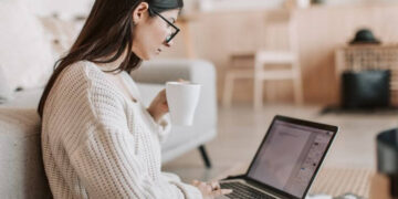 Foto de uma mulher usando um laptop e segurando uma xícara, representando um tutorial sobre como postar no Instagram pelo PC em 5 minutos.