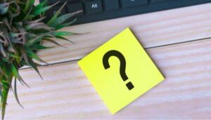 Foto de um post-it amarelo com um ponto de interrogação em cima de uma mesa de madeira, representando a formulação de perguntas e estratégias para o Instagram.