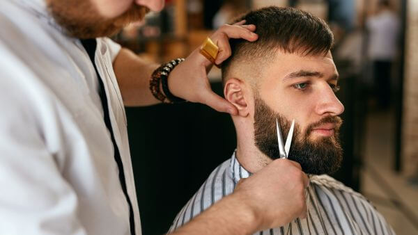 Barbeiro profissional ajustando cuidadosamente a barba de um cliente em um ambiente de barbearia.